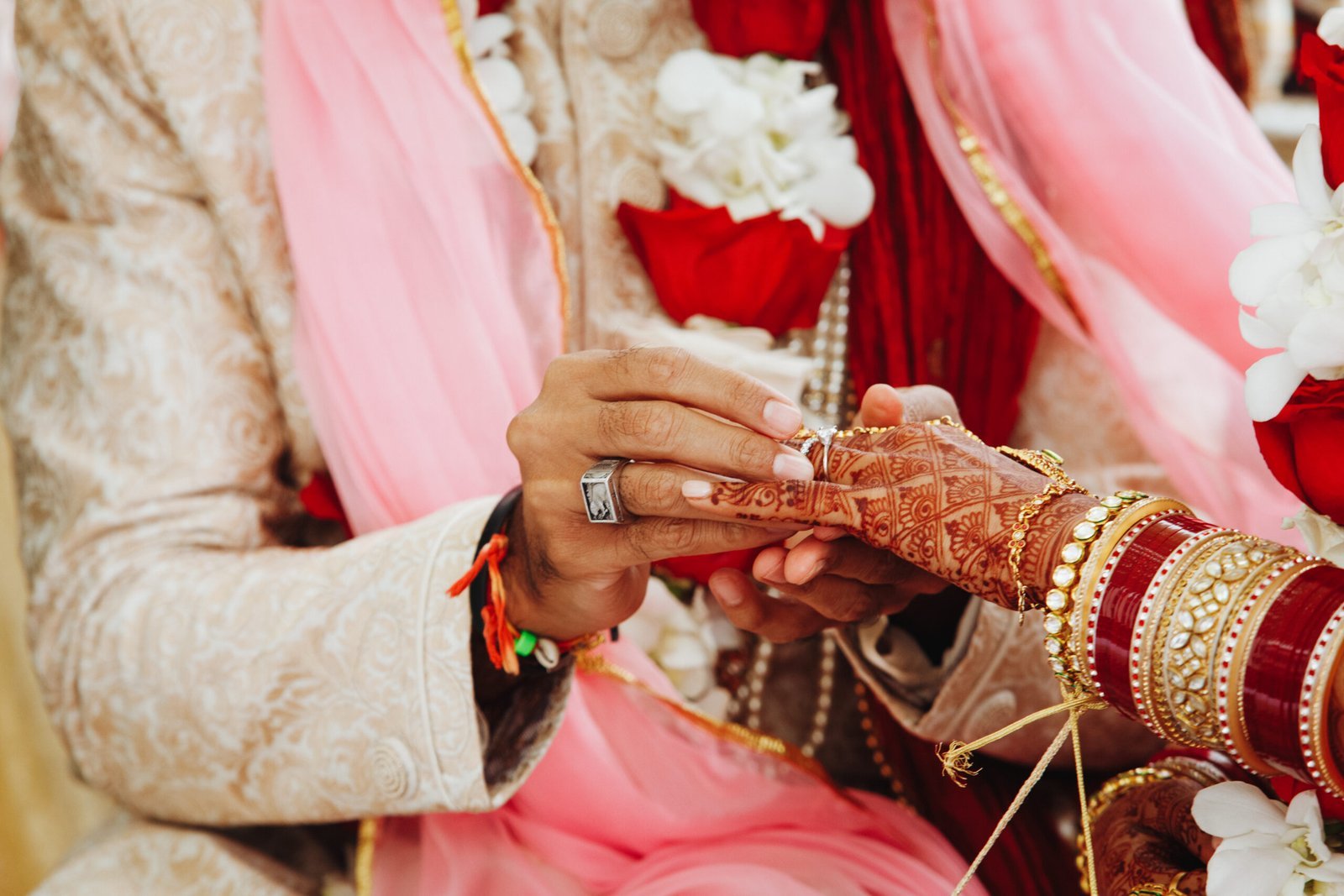 Close-up of a couple exchanging rings during a traditional wedding, hands adorned with henna, bangles, and ornate attire.